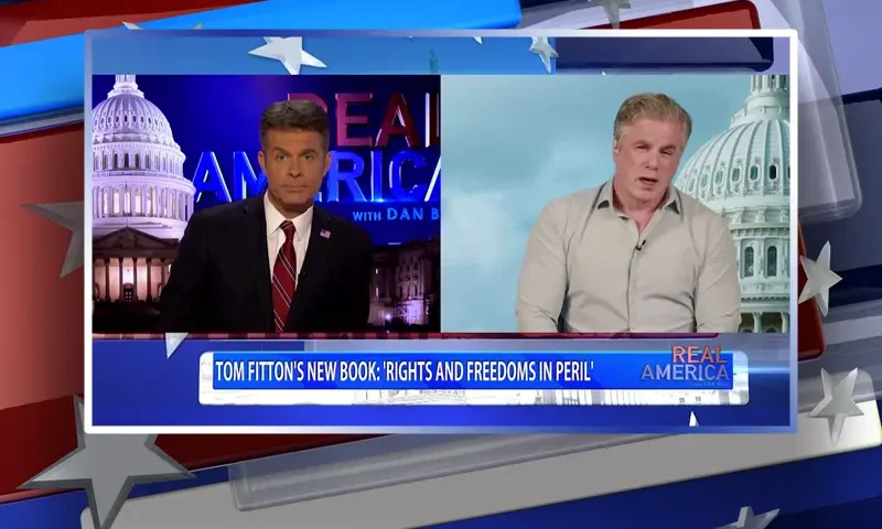 Video still from Real America on One America News Network showing a split screen of the host on the left side, and on the right side is the guest, Tom Fitton.