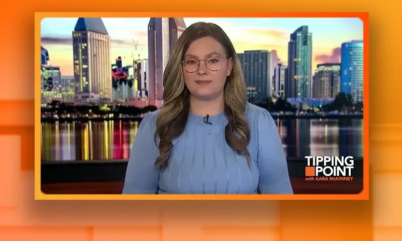 Video still of the host of Tipping Point at the desk of their talk show on One America News Network.