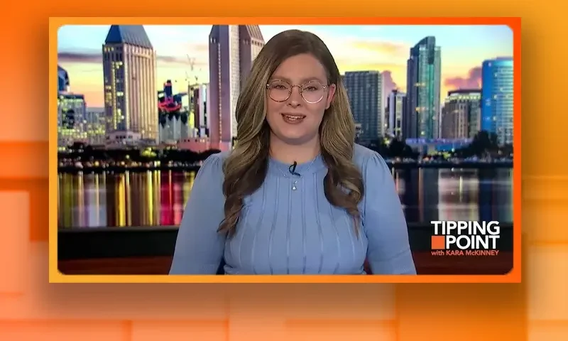 Video still of the host of Tipping Point at the desk of their talk show on One America News Network.